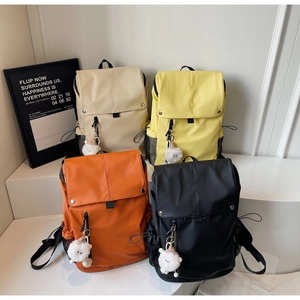 Detail view of colorful nylon backpacks in beige, yellow, orange and black with cute charms