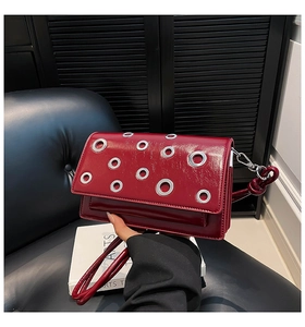 Detail view of burgundy glossy leather crossbody bag with silver metal eyelet hardware