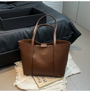 Dettaglio di una borsa tote in ecopelle marrone scuro con logo dorato e spalline lunghe