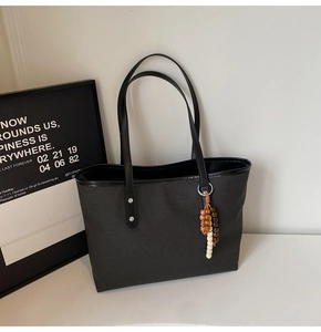 Close-up of black canvas tote bag with long leather handles and vintage beaded charm