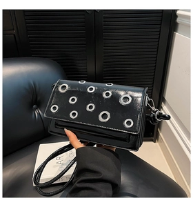 Detail of a black patent leather shoulder bag with silver eyelets and polished finish