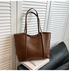 Dettaglio borsa tote in pelle marrone con logo dorato posata su un libro bianco