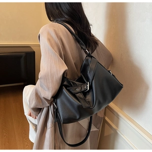 Rear view of model wearing a black pebbled leather tote bag with a metallic buckle detail