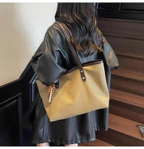 Detail of canvas tote bag with brown leather handles and decorative beaded tassel