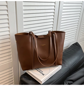 Borsa tote in pelle marrone con logo dorato su libri davanti a uno sfondo di persiane