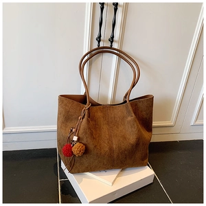 Detail of a brown suede tote bag featuring a decorative plush ball charm and long straps