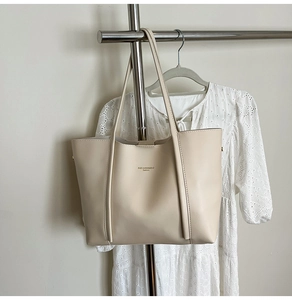 Dettaglio della borsa tote in pelle bianco panna con spalline lunghe su una parete pulita