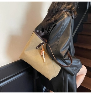 Model wearing a large khaki tote bag with dark brown leather handles and bead charm