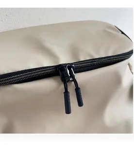 Close-up of smooth double black zippers and nylon fabric detail on beige backpack