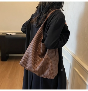 Side view of a brown woven leather tote bag carried by a model in a minimalist room