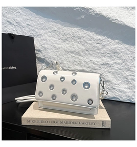 Detail of white leather baguette bag with silver metal eyelets on art book background