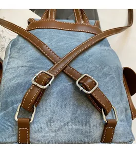Close-up of washed blue denim backpack with brown leather straps and metal buckles