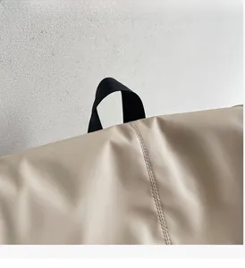Macro detail of the beige nylon backpack showing durable black handle and stitching