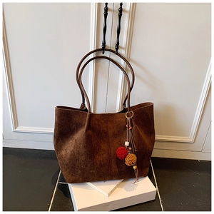 Detail of dark brown faux suede tote bag with plush ball charms and leather tassel accents