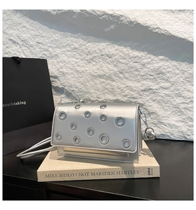 Detail of silver baguette bag featuring circular metal eyelets and a mirror finish leather