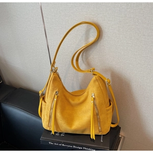 Detail of yellow faux suede shoulder bag featuring long tassel zipper pulls on a book