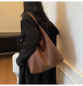 Detail shot of a dark caramel woven leather tote bag worn as a shoulder bag on a model