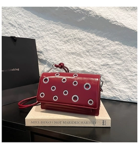 Detail of burgundy leather baguette bag with silver metal eyelets on artistic backdrop