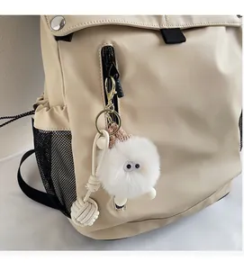 Detail of a white fluffy monster keychain with big eyes attached to a beige backpack