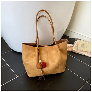 Close-up of brown suede tote bag with elegant dual-tone pompom charm and thin handles