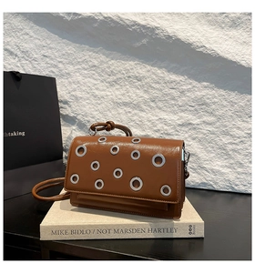 Brown leather baguette bag featuring silver grommet eyelets and a knotted handle detail