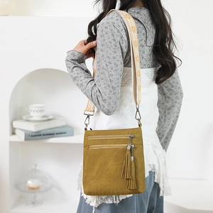 Detail view of mustard crossbody bag with dual zippers and ethnic woven shoulder strap