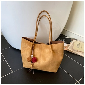Close-up of brown suede tote bag with stylish pompom tassel and sleek long shoulder straps