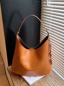 Caramel brown large hobo shoulder bag with wooden bead charm in artistic sunlight shadow