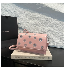 Detail of pink faux leather crossbody bag with silver grommets on a minimalist background