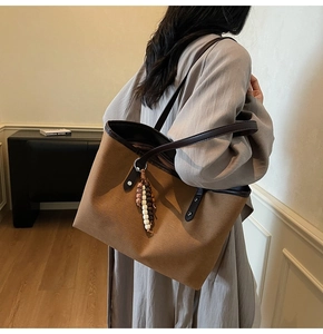 Detail of a brown tote bag with leather handles and a beaded tassel charm for work