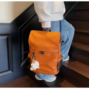 Detail of a bright orange nylon backpack featuring silver studs and a cute plush charm