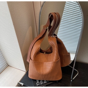 Détail du sac seau marron en cuir tressé avec large bandoulière sur support moderne