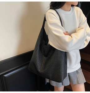 Close-up of a large black woven tote bag showing the intricate interlaced texture on the strap