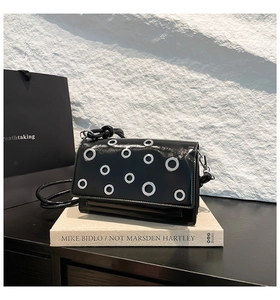Detail of black glossy baguette bag with silver grommets on a stack of books