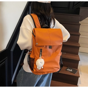 Detail of orange nylon backpack featuring a mesh side pocket and soft plush pendant accessory