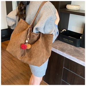 Close-up of brown suede tote bag with decorative colorful pom-poms on shoulder strap