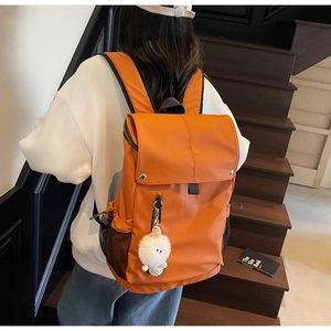 Detail of bright orange nylon backpack with plush charm and mesh side pockets on a model