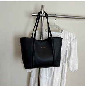 Dettaglio della borsa tote in pelle nera opaca con logo dorato in rilievo sull'asta