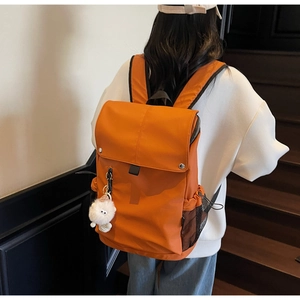 Detail of orange nylon backpack with plush bear charm and side mesh pocket shown on shoulder