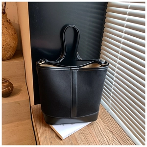 Close-up of black frosted suede bucket bag with leather strap on a wooden surface