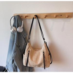 Detail showing beige suede tote with metal zippers and elegant black tassel accents