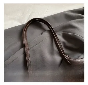 Close-up of brown leather tote bag with silver metal rings and braided handle detail