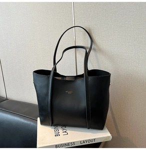 Dettaglio della borsa tote minimalista in pelle nera con logo dorato su libri bianchi