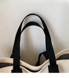 Detail of canvas tote bag with black webbing straps, stripe lining and zipper closure