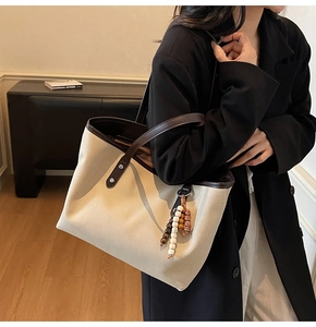 Detail view of canvas tote with brown leather trim and bohemian beaded charm on a model