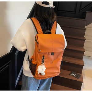 Rear view of model wearing an orange large-capacity nylon backpack with a plush pendant