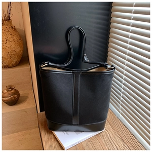 Close-up of black bucket bag featuring canvas and matte leather trim with gold hardware