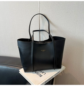 Dettaglio della borsa tote in pelle nera con logo dorato su libri decorativi bianchi