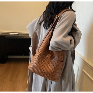 Détail du sac seau marron en cuir tressé avec bandoulière réglable et texture de qualité