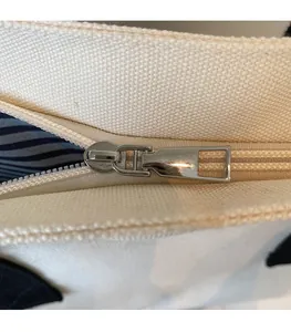 Detail of silver metal zipper and blue striped lining on off-white canvas tote bag